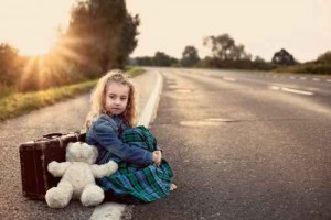 Lonely child with a suitcase and a teddy bear on road