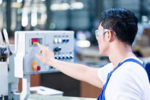 Worker pressing buttons on CNC machine in factory